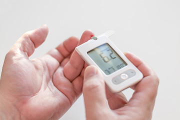 Medicine, diabetes, glycemia, health care and people concept - Close up of man hands testing high blood sugar level with glucometer or glucose meter and test stripe at home