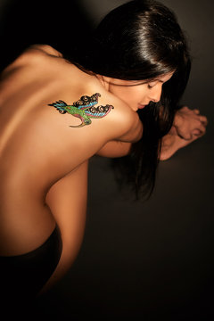 Black-haired half naked girl with colored temporary tattoo painted with paints for body art. Hummingbird pattern.