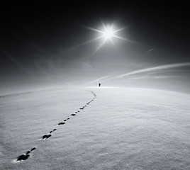 Earth. Universe.Lonely man walking on snow crust field on the trail of a hare on the background of...