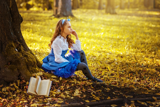 Girl schoolgirl at the image of Alice in Wonderland with a book under a big tree.