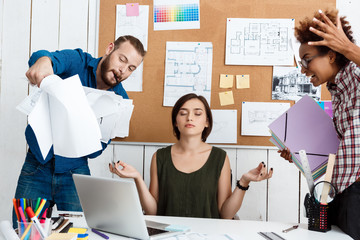 Colleagues argueing,  discussing drawings, new ideas while girl meditating. Office background.