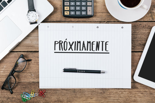Proximamente, Spanish text for Coming Soon on note pad at office desk with computer technology, high angle