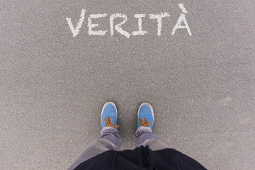 Verita, Italian text for Truth text on asphalt ground, feet and shoes on floor