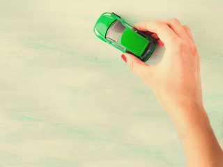 Toy child car in woman's hand. Top view on bright wooden textured background. Purchase insurance bank loan travel where to go trip journey concept. Toned