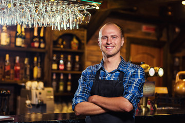 Barman at work in pub,Portrait of cheerful barman worker standing,Waiter giving menus,A pub.Bar.Restaurant.Classic.Evening.European restaurant.European bar.American restaurant.American bar.