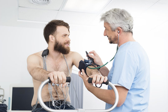 Doctor Measuring Blood Pressure Of Patient Cycling In Hospital