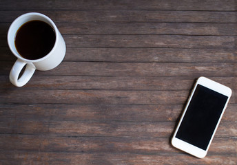 White coffee cup and white smartphone on rustic wooden table.