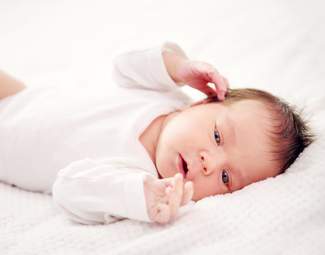 Cute newborn baby girl lying in the bed. Two weeks old infant child on white soft blanket