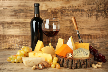Naklejka premium Red wine and stump with variety of cheese on wooden background
