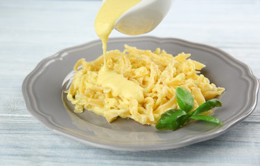 Adding cheese sauce to delicious pasta on wooden background