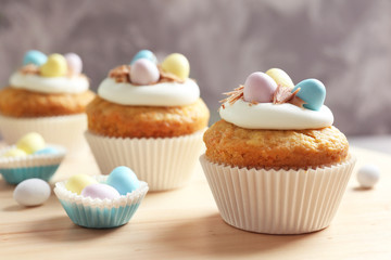 Decorated Easter cupcakes on wooden table against grey background