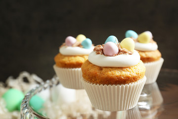 Tasty Easter cupcakes on glass cake-stand against dark background