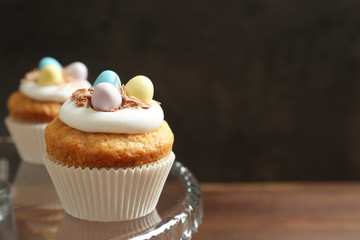 Decorated Easter cupcakes on glass cake stand against dark background