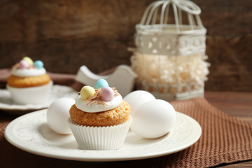 Delicious Easter cupcake on white plate against wooden background