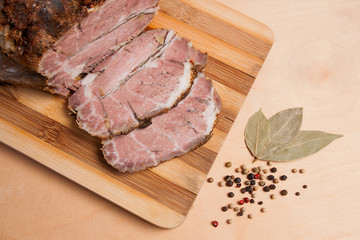Sliced baked pork with herbs and spice on wooden board.
