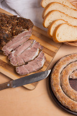 Roasted traditional homemade sausage with spices and herbs. Baked pork with herbs and spice on wooden board and and slices white wheat bread.
