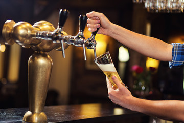 Bartender pouring the fresh beer in pub,barman hand at beer tap pouring a draught lager beer,beer...