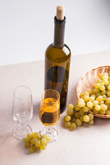 White wine and grapes. White wine in glass with bottle and grapes on light marble background.