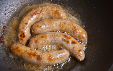 Sausages in a natural shell are fried in a frying pan