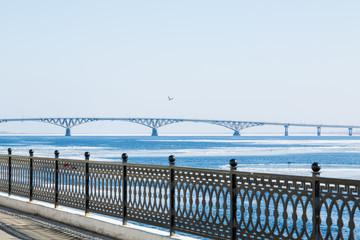 The spring ice drift on the river Volga. Road bridge in the city of Saratov. Russia. A Sunny day in March. Blue sky. Cast iron fence on the waterfront.