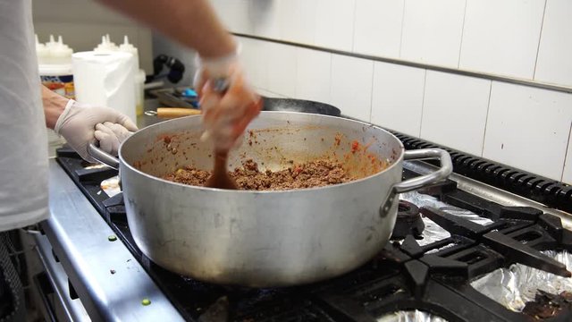 A male cook adding tomatoes in the meat sauce, 4K