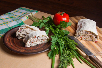 Two pieces of pita bread or lavash roll with cottage cheese or curd, chicken, tomatoes and herbs - dill, onion, parsley on brown clay plate..