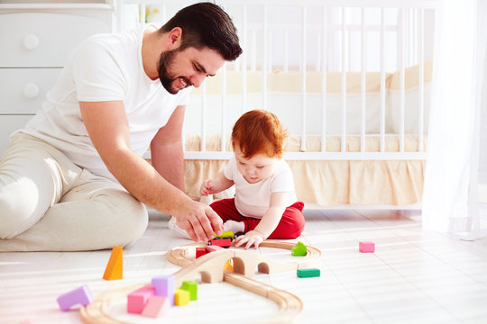 happy father playing with infant baby boy at sunny nursery room