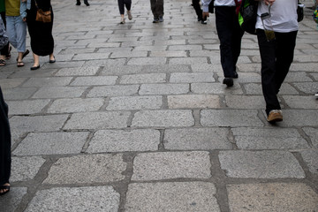 People walking on sidewalk, ancient stone pavement, oled square rock floor.