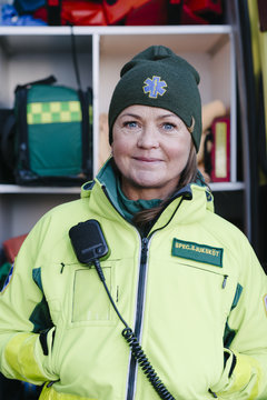 Portrait of confident female paramedic in reflective clothing standing against ambulance