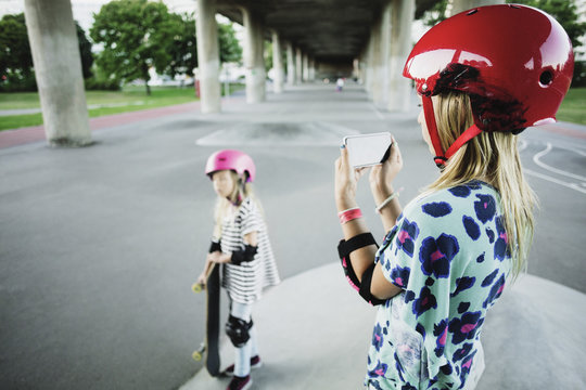 Girl photographing friend through smart phone at skateboard park