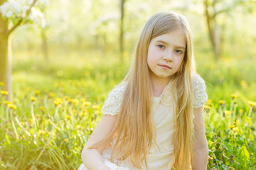 Fototapeta premium A beautiful little girl runs through a flowering garden in the spring