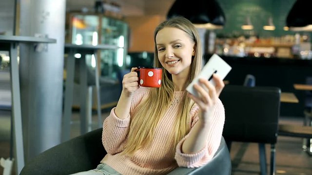 Happy girl holding vintage mug and doing selfies on smartphone in the cafe
