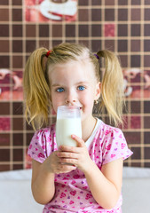 Девочка в розовой майке пьет молоко из стакана.