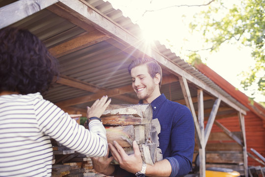 Rear view of woman giving logs to smiling male friend during sunny day