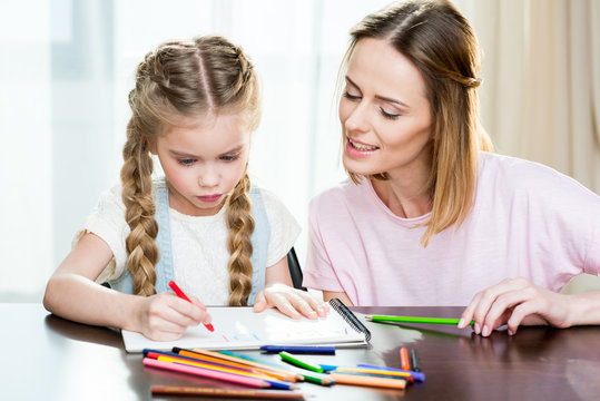 Happy mother and daughter drawing at home