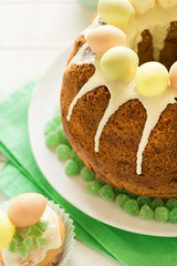 Glazed Easter cake decorated candy eggs on white wooden table. Selective focus

