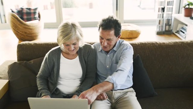 Senior couple with laptop sitting on a couch in living room