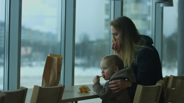 Small son and mom eating french fries in a cafe and looking out the window.