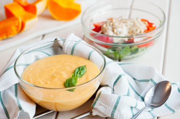 Pumpkin cream soup with basil and pumpkin slice on wooden background