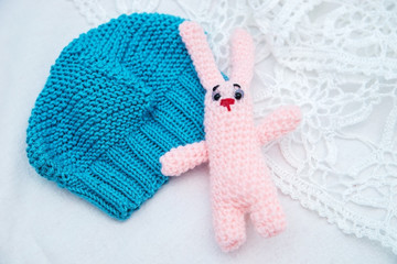 Baby items: blue knitted spring hat and toy rabbit handmade white blanket.