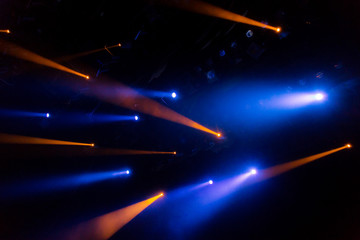 The blue-yellow light from the spotlights through the smoke in the theatre during the performance. Lighting equipment.