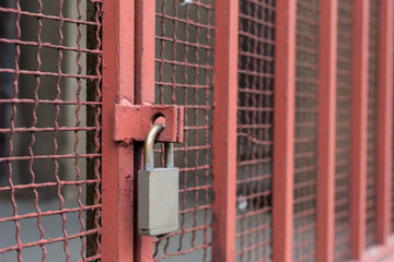 Closed silver lock hanging on red lattice guards industrial background