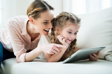 portrait of cheerful mother and daughter using tablet at home - Powered by Adobe