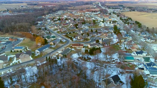 Small town American neighborhood at dusk in March, with a smattering of snow, aerial view.