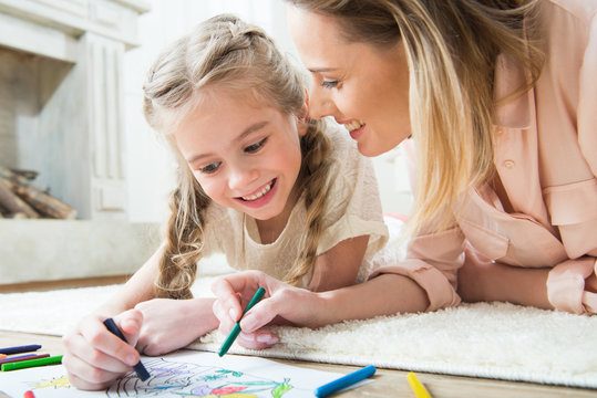 portrait of happy daughter drawing with mother at home
