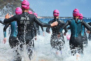 Group triathlon participants running into the water for swim portion of race,splash of water and...