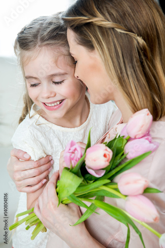 side view of happy mother with tulips hugging smiling daughter, mother's day concept