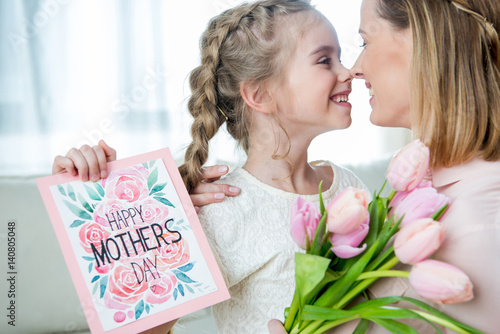 side view of smiling daughter greeting mother with tulips and postcard on mother's day