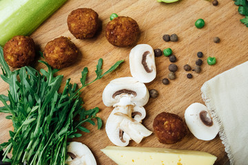 Vegetarian falafel and fresh green vegetables and mushrooms on a wooden board