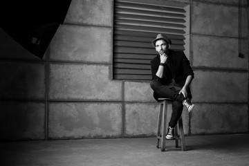 Fototapeta na wymiar Stylish model guy in black and white hat sits on a high chair